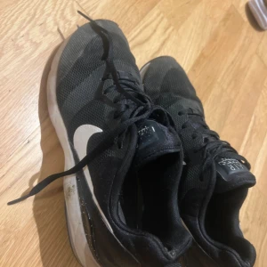 Svarta Nike Air sneakers med vit sula - Svarta Nike Air sneakers med vit sula och klassisk vit swoosh på sidan. Ovandelen är i mesh för bra andningsförmåga och skon har snörning. Perfekta för dig som gillar sportig stil och vill ha bekväma skor till vardagen.