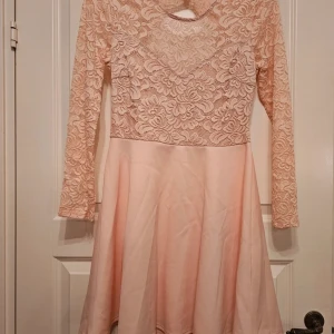 Ljusrosa spetsklänning från NLY One - Superfin ljusrosa kortklänning från NLY One med långärmade spetsdetaljer upptill och slät kjol. Klänningen har rund halsringning och vackert blommönster i spetsen. Öppen rygg.  Perfekt för dig som gillar romantisk och feminin stil. Kjolen är av lite tjockare tyg.  Förstärkt tyg över magen och byst.  Hitta en liten fläck på kjolen