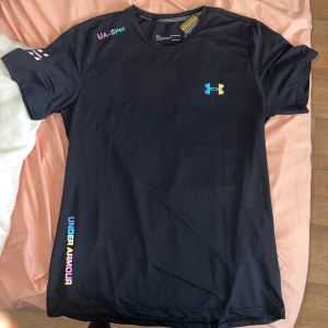 Under Armour t-shirt och shorts med reflektiv logga - Svart t-shirt och shorts från Under Armour med reflektiv logga på bröstet och tryck på ärmen och sidan. Tillverkad i lätt och snabbtorkande polyester, perfekt för träning. Klassisk rund hals och korta ärmar. Snygg och sportig vibe. Storleken är XL men sitter som L. Passar dig som är 185cm+. Det är bara skriva om ni vill ha fler bilder. Skickas inom en 1-2 dagar.