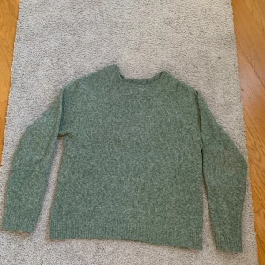 Grön stickad tröja från Vero Moda - Mysig grön stickad tröja från Vero Moda i storlek S. Tröjan har en klassisk rund halsringning, långa ärmar och ribbade muddar vid ärmslut och nederkant. 