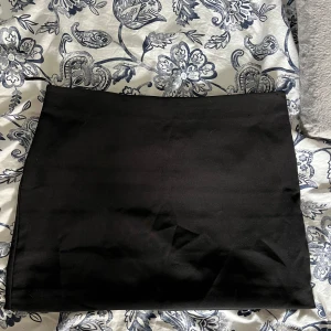 Svart kortkjol från Gina Tricot - Enkel och stilren svart kortkjol från Gina Tricot i storlek 36. Kjolen har rak passform och är tillverkad i ett slätt, mjukt tyg. Perfekt att matcha med en crop top eller oversized tröja för en clean look.