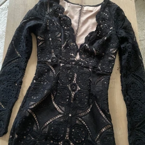 Svart spetsklänning från Love Triangle - Supersnygg svart kortklänning från Love Triangle med långärmade ärmar och genombruten spets över nude-färgad underklänning. Klänningen har figurnära passform och v-ringning. För liten för mig så kan inte prova den längre.