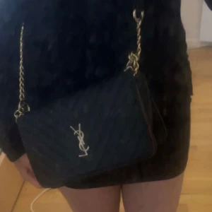 Svart quiltad YSL axelväska i skinn - Säljer en svart axelväska från YSL med klassisk guldlogga framtill. Väskan är quiltad och har en kedjerem i guld. Tillverkad i skinn och har en stilren, rektangulär form som passar perfekt till din outfit.