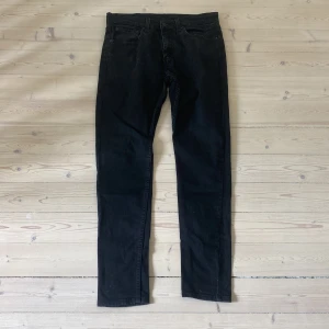 Levi's 512 svarta jeans W32 L34 - Svarta Levi's 512 jeans med slim passform och klassisk femficksdesign. Jeansen har en snygg, mörk tvätt och är tillverkade i mjukt bomullstyg med lite stretch för extra komfort. Perfekta för dig som gillar en modern och stilren look.