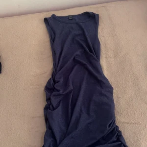 Mörkblå glittrig ärmlös klänning - Snygg mörkblå ärmlös klänning med glittrigt tyg och figurnära passform. Klänningen har rynkade detaljer längs sidorna som ger en cool och trendig look. Perfekt för dig som vill sticka ut med stil och glitter.