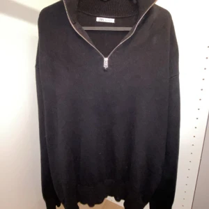 Svart stickad half zip-tröja från Zara - Svart stickad tröja från Zara i storlek L med hög krage och half zip-dragkedja. Oversized passform och långa ärmar, perfekt för lager-på-lager. Ribbad krage och muddar ger en clean och stilren look. Den passar dig som är mellan M-L. Skriv till mig om du har några funderingar.