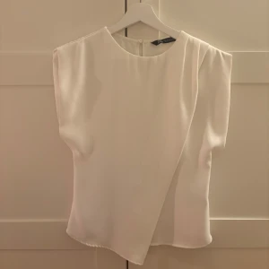 Vit blus från Zara - Säljer denna fina stilrena vita blusen från Zara😍 blusen har en fin asymmetrisk drapering framtill! Sparsamt använd och är i nyskick💕