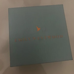 Emily Westwood smyckeset med blommor - Säljer ett smyckeset från Emily Westwood med ring, halsband och örhängen. Alla delar har en söt vit blomformad detalj med guldfärgad kant. Perfekt för dig som gillar stilrena och feminina accessoarer. Kommer i originalask. Aldrig använda, kan också ge pris förslag.