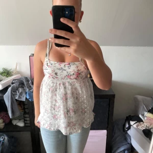 Blommig linnetopp från WeTweens - Supersöt linnetopp med blommigt mönster i vitt, rosa och grönt från WeTweens(Kappahl). Toppen har tunna axelband och ett luftigt, lätt material som känns perfekt för varma dagar. Volangkant nertill och romantisk vibe. Perfekt att styla med jeans eller shorts!