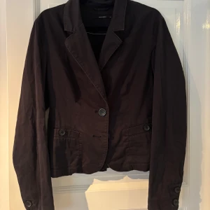 Svart kavaj från Vero Moda, stl 42 - Stilren svart kavaj från Vero Moda i storlek 42. Klassisk design med två knappar framtill, fickdetaljer och snygg knappdekor bak. Långärmad och tillverkad i bomullsmaterial som känns bekvämt och lätt. Perfekt för dig som vill ha en clean och tidlös look.