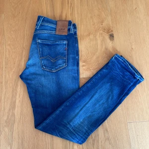 Replay Anbass Hyperflex jeans - Snygga Replay Hyperflex jeans i klassisk blå tvätt med lätt slitning och skinny fit. Jeansen har fem fickor, tydliga sömmar och läderpatch bak i midjan. Stretchigt material som ger skön passform och rörelsefrihet. Perfekta för dig som gillar en modern och smal siluett. Skriv vid funderingar!