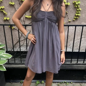 Grå klänning - Supersöt grå kort klänning med tunna axelband och rynkad överdel. Klänningen har en luftig passform och faller snyggt, perfekt för varma dagar. Enkel och stilren design som känns både trendig och bekväm.