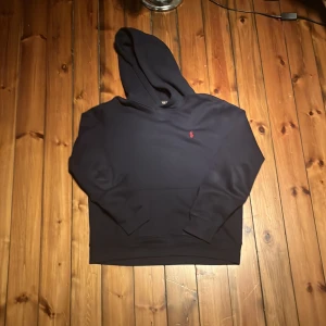 Mörkblå hoodie från Polo Ralph Lauren - Snygg mörkblå hoodie från Polo Ralph Lauren med klassisk huva och liten röd logga broderad på bröstet. Tröjan är i mjuk bomull och har en relaxed passform med långa ärmar. Perfekt för chill dagar eller när du vill ha en clean och stilren look. Storlek XL i barn 18-20år kom gärna med frågor och pruta för en snabb affär