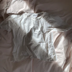 Vit blus med broderi från Zara - Supersöt vit blus från Zara med puffiga korta ärmar och broderade detaljer vid axlarna. Tillverkad i mjuk bomull och har en avslappnad passform. Perfekt för dig som gillar en romantisk och stilren look.