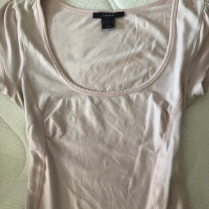 Ljusrosa topp från Gant - Supersöt ljusrosa topp från Gant med rund, djup urringning och korta ärmar. Tillverkad i mjuk bomull som känns skön mot huden. Perfekt för dig som gillar en enkel men stilren look.