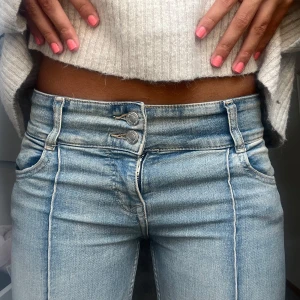 Ljusblå bootcut jeans low rise - Snygga ljusblå jeans med bootcut passform och markerade pressveck längs benen. Jeansen har dubbla knappar i midjan, klassiska fickor fram och bak samt en lätt tvättad look. Perfekta för dig som gillar en retro vibe och vill ha ett par jeans som sticker ut. 