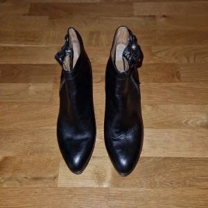 Svarta klackade boots Acne Studios - Snygga svarta boots från Acne Studios i äkta skinn med hög klack och plattform. Skorna har rund tå, dragkedja på sidan och coolt spänne med nitar vid ankeln. Perfekta för dig som vill ha en stilren men edgy look.