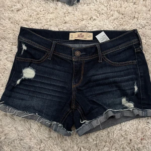 Mörkblå jeansshorts från Hollister - Snygga mörkblå jeansshorts från Hollister med slitna detaljer , är lågmidjade på mig, 39cm I midjemått rakt över