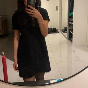 Svart kort boucléklänning - Säljer en svart kort klänning i bouclé-liknande material från Zara med korta ärmar och råa kanter. Klänningen har en rak passform och dragkedja bak. Perfekt för dig som gillar en stilren look med lite textur. Storleken på klänningen är M men klänningen passar egentligen inte någon med storlek M utan jag skulle säga att den passar XS/S.