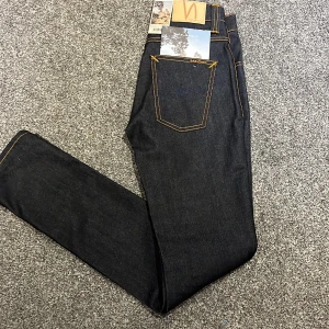 Nudie Jeans Grim Tim Dry Navy W28 L32 - Säljer ett par Nudie Jeans Grim Tim i färgen Dry Navy. Jeansen har klassisk femficksdesign, raka ben och kontrastsömmar i orange. Tillverkade i mörkblå, rå denim av bomull. Snyggt läderpatch bak i midjan och diskret logga på bakfickan.