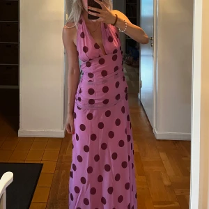 Lång prickig rosa klänning (Viral Zara polka dress) - Säljer en lång, rosa klänning med stora mörklila prickar. Klänningen har djup v-ringning, halterneck och öppen rygg. Sitter snyggt och har en flowy passform som ger en riktigt cool vibe. Perfekt för dig som vill sticka ut med ett lekfullt mönster.