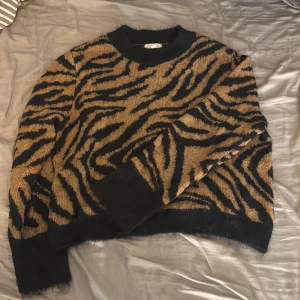 Zebramönstrad stickad tröja - Säljer en stickad tröja med zebramönster i svart och beige. Tröjan har rund halsringning, långa ärmar och ribbade muddar vid ärmslut och nederkant. Perfekt för dig som vill sticka ut med ett djurmönster i höst och vinter.