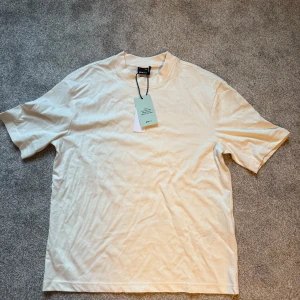 Oversized t-shirt med Paris-tryck Gina Tricot - Snygg oversized t-shirt från Gina Tricot i ljus beige färg. Framsidan har ett coolt tryck med texten 'DINNER IN PARIS' och en minimalistisk illustration av ett bord och två stolar. T-shirten är kortärmad och gjord i mjuk bomull. Perfekt för en chill och trendig look.