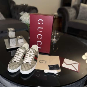 Gucci GG Supreme sneakers med röd/grön rand - Gucci sneakers i GG Supreme canvas med klassisk röd och grön rand på sidan. Beige och brunt monogrammönster, vita snören och vit sula. Baksidan har grönt skinn med guldfärgad Gucci-logga. Snygg och tidlös modell med rund tå och platt sula.