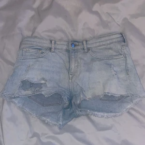 Ljusblå jeansshorts från H&M - Säljer ett par ljusblå jeansshorts från H&M i storlek 36. Passar folk som bär 38/M, beror på hur tajt man vill ha de. De har fransiga kanter och slitna detaljer framtill för en avslappnad vibe. Perfekta för varma dagar. Använd flera gånger men säljer då de är för stora för mig nu 💕