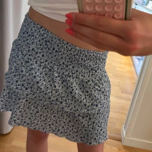 Blommig kortkjol med volang - Supersöt kortkjol med blått blommönster på ljusblå botten. Kjolen har smock i midjan för en bekväm passform och volang nertill som ger en extra gullig touch. Perfekt för varma dagar och enkel att matcha med en enkel topp. Är i storlek 134/140 men passar mig som är 164 så den passar typ alla på grund av dens smock i midjan ❤️kan också användas som tubtopp. Kontakta mig vid frågor 🥰