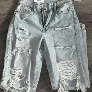 Mom jeans high waist + prislapp  - Säljer ett par ljusblå mom jeans från H&M med ultra hög midja och rejält slitna detaljer framtill. Jeansen har klassisk femficksdesign, dragkedja och knapp, och är tillverkade i bomull. Perfekta för en avslappnad och trendig look.
