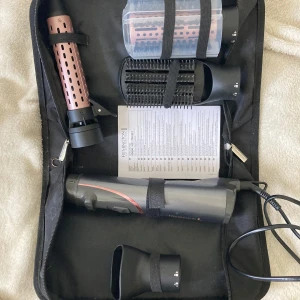 Remington stylingverktyg i väska - Remington stylingverktyg med flera utbytbara borsthuvuden och tillbehör, allt i en svart väska. Verktyget är svart med roségulddetaljer och har olika munstycken för styling. Perfekt för att fixa håret hemma med proffsig känsla.