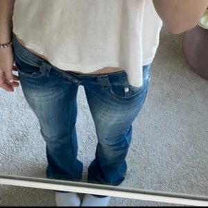 Lowwaist jeans bootcut - Säljer ett par blå jeans med snyggt slitna detaljer och bootcut-ben. Jeansen har låg midja, tre knappar i gylfen och klassisk femficksdesign.  En av knapparna har gått av men det kan man enkelt fixa, lite små defekter vid benen men det är inget man tänker på!💞