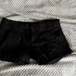 Svarta kostym shorts - Snygga svarta shorts med klassisk passform och uppvikta ben. De har hällor för bälte, knapp och dragkedja framtill samt fickor både fram och bak. Nya och oanvända