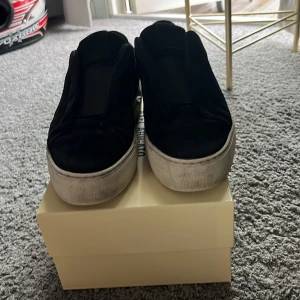 Svarta sneakers från Axel Arigato - Snygga svarta sneakers från Axel Arigato med chunky vit platt sula. Ovandelen är i mocka och skon har en stilren slip-on design utan snörning. Perfekta för dig som gillar minimalistisk och modern stil.