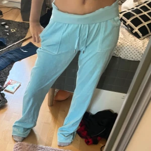 Ljusblå mjukisbyxor från Juicy Couture - Säljer ett par ljusblå mjukisbyxor från Juicy Couture. Byxorna har en bekväm passform med elastisk midja och snörning. De har praktiska fickor både fram och bak, vilket ger en avslappnad look. Perfekta för en chill dag hemma eller en avslappnad utflykt.