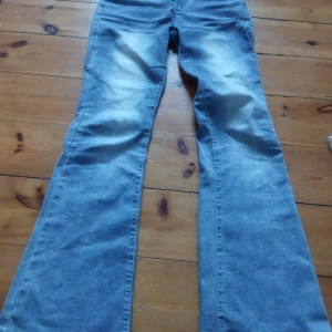 Blå bootcut jeans - Säljer ett par snygga blå bootcut jeans med dekorativa bakfickor. Jeansen har en klassisk femficksdesign och knappgylf. Perfekta för en avslappnad stil.