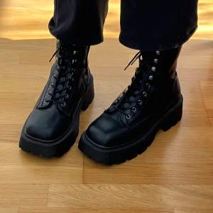 Snygga svarta boots med kraftig sula och snörning. Perfekta för en tuff look och passar bra till både jeans och kjol. De har en robust design med metallöglor för snörningen.