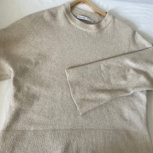 Beige tröja från Bershka - Säljer en stilren beige stickad tröja från Bershka. Tröjan har en rund halsringning och långa ärmar med ribbade muddar. Perfekt för en avslappnad look.