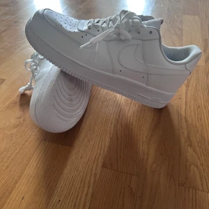 Vita Nike Air Force sneakers - Säljer ett par klassiska vita Nike Air Force sneakers. De har en stilren design med snörning och perforerade detaljer på tån för extra ventilation. Perfekta för en casual look.
