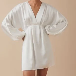 Vit klänning med v-ringning - Elegant vit klänning med v-ringad design och långa ärmar. Tillverkad i ett mjukt och flödande material som ger en lyxig känsla. Klänningen är väldigt stretchig och bekväm. Perfekt som studentklänning!