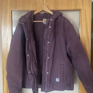 Lila jacka från Carhartt - Säljer en snygg lila jacka från Carhartt med huva och dragkedja. Jackan har en mysig fleecefoder och praktiska fickor. Nytvättad✨