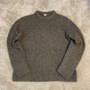 Arket Stickad Ull/Alpacka Tröja - Säljer en stilren grå stickad tröja från Arket. Tröjan har en klassisk design med ribbade muddar och en mjuk textur. Perfekt för kyliga dagar och enkel att matcha med olika outfits. Passar både till vardag och mer uppklädda tillfällen. Lite nopprig men inget som syns. Gråbrun färg.