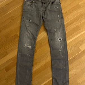 Jacob Cohen jeans modell Nick - Snygga grå jeans från Jacob Cohen med slitna detaljer och knappgylf. Tillverkade i Italien, dessa jeans har en modern look med en touch av vintage. Perfekta för dig som gillar en stilren men avslappnad stil. De är väldigt sällsynta och exklusiva. Modellen är nick vilket är slim. Skriv om ni har några funderingar.