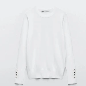 Vit tröja från Zara med knappar - Säljer en stilren vit tröja från Zara med långa ärmar och dekorativa knappar vid ärmsluten. Perfekt för en elegant och minimalistisk look. Tröjan har en rund hals och är tillverkad i ett mjukt material.