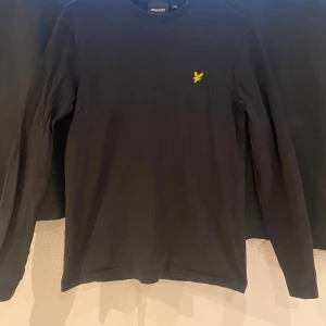 Svart långärmad t- tröja från Lyle & Scott - Säljer en stilren svart långärmad t- tröja från Lyle & Scott med deras ikoniska gula logga på bröstet. Perfekt för en avslappnad och snygg look. Passar bra till både jeans och chinos. Haft den i cirka ett år och den är inte använd så många gånger. Den är i väldigt fint skick!