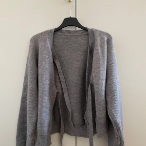 Grå kofta  - Säljer en mysig grå kofta från SHEIN med knytband framtill. Koftan har långa ärmar och är perfekt för kyligare dagar. Har knappt använt den