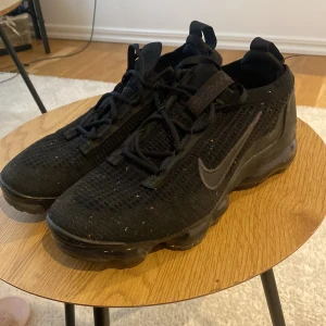 Svarta Nike Vapormax sneakers - Säljer ett par svarta Nike Vapormax sneakers med stickad ovandel och snörning. Skorna har en unik sula med synliga luftkuddar för extra komfort. Perfekta för både träning och vardag.