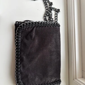 Svart axelväska med kedjedetaljer - Snygg svart axelväska med kedjedetaljer och en unik kantdesign. Perfekt för att ge din outfit en edgy touch. Väskan har en stilren look och passar till många olika stilar.