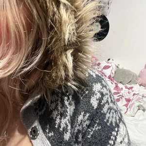 Grå mönstrad kofta från H&M - Säljer en mysig grå kofta från H&M med ett snyggt mönster i olika grå nyanser. Koftan har en huva med fuskpäls och knäppning framtill. Perfekt för kyliga dagar!